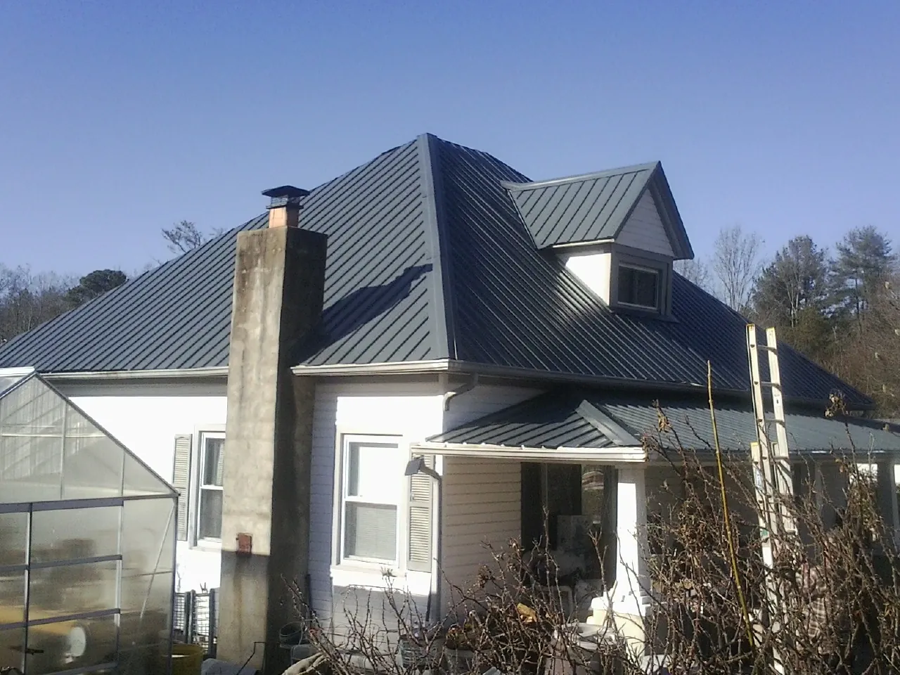 Dark blue standing seam metal roof on a white farmhouse with dormer — Slate & Tile Roof Repair by Roofing Brothers in Wading River