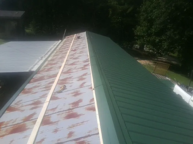 Old rusted panels beside newly installed green metal roofing — Wind Damage Roof Repair by Roofing Brothers in Wading River