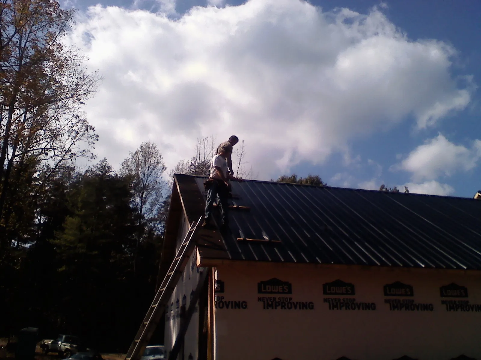 Roofer fastening dark metal panels high against a cloudy sky, from a Roof Inspection job in Wading River